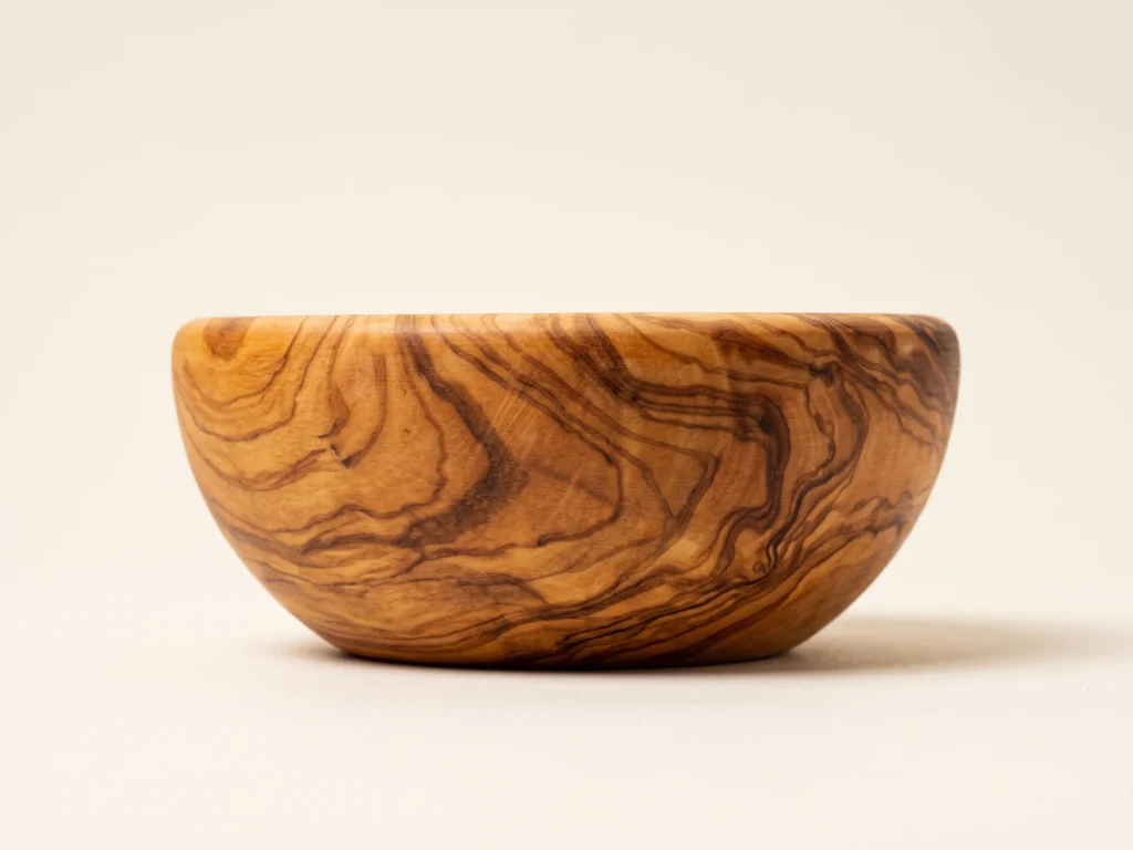 Side elevation view of round smooth olive wood bowl showing curved silhouette and flat base