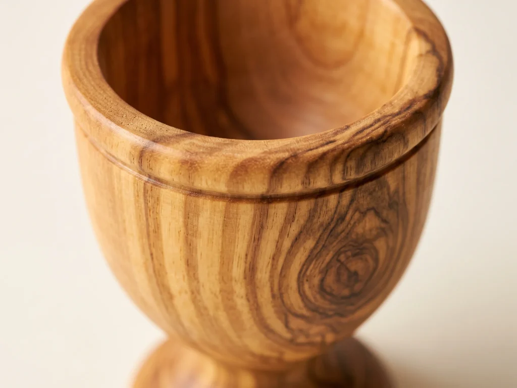 Macro close-up of olive wood egg cup TR-22 chalice rim, decorative accent groove, and dense timber grain ribbons