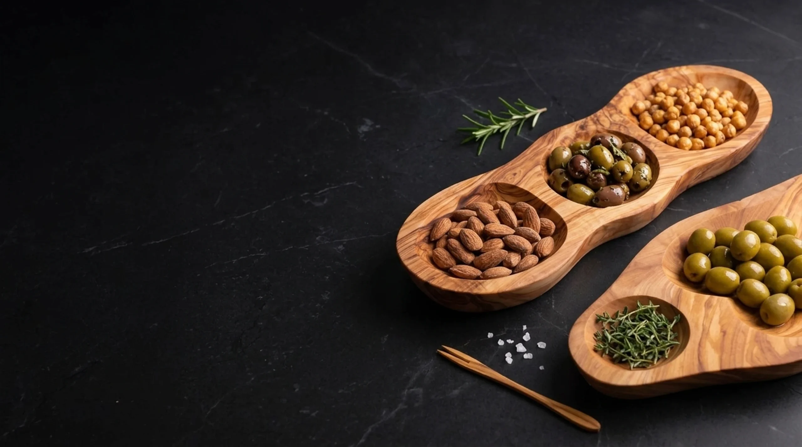 Handcrafted olive wood sculpted appetizer platter and olive dish with mezze on dark charcoal slate