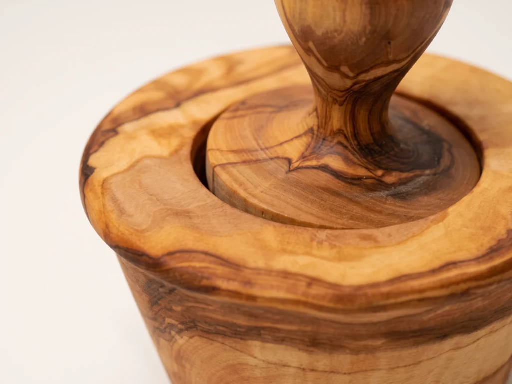 Macro close-up of wide flat crushing disc of garlic pestle and dense olive wood grain on mortar TR-10