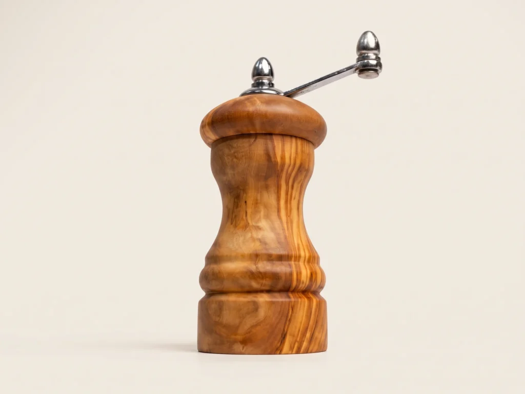 Vue rasante en contre-plongée du mini moulin TR-40 soulignant le galbe compact du bois d'olivier et l'élévation de la manivelle