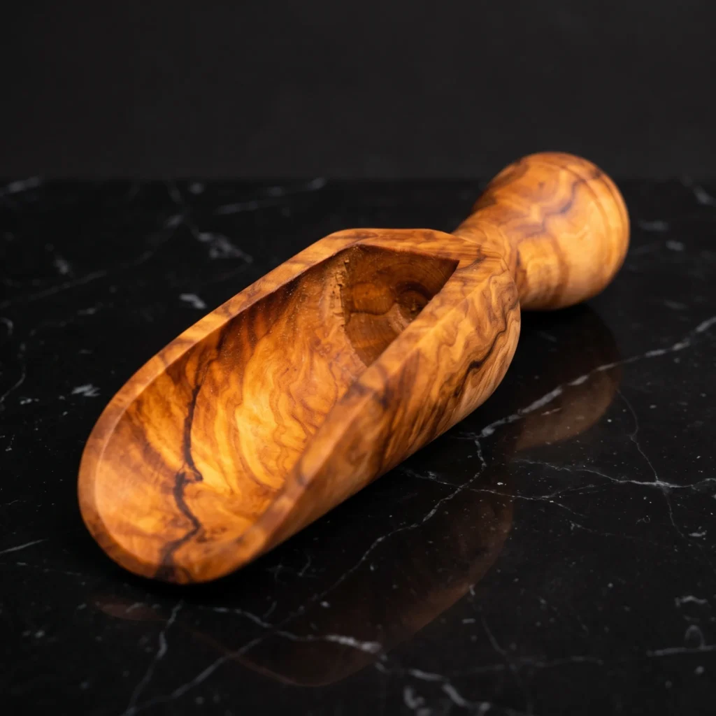 Handcrafted olive wood spice scoop TR-23 on polished black Nero Marquina marble with carved chute and bulbous handle
