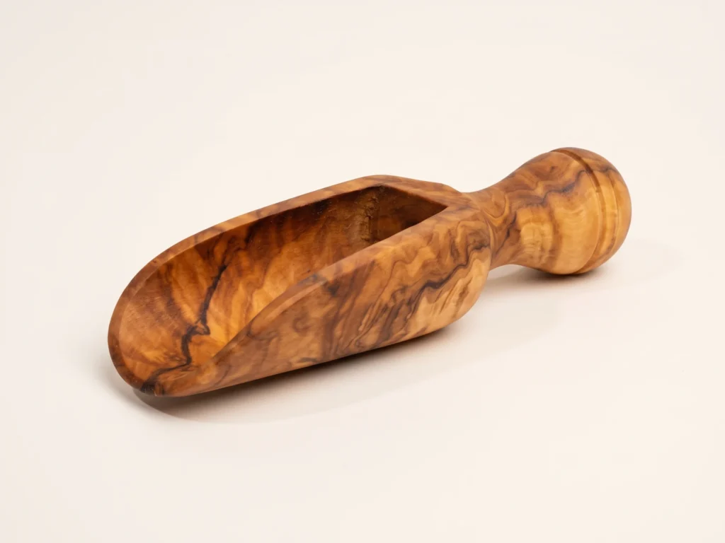 Olive wood spice scoop TR-23 three-quarter perspective on neutral light background showing carved U-chute and turned handle