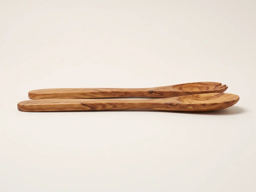 Low-angle profile grazing view of olive wood salad servers documenting slim flat shape and 1.0 cm handle thickness