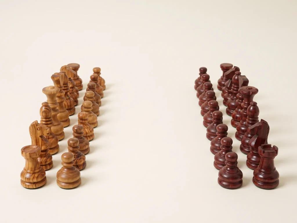 Vue d'ensemble en perspective trois-quarts basse des pièces d'échecs artisanales en bois d'olivier en rangs d'affrontement sur fond ivoire