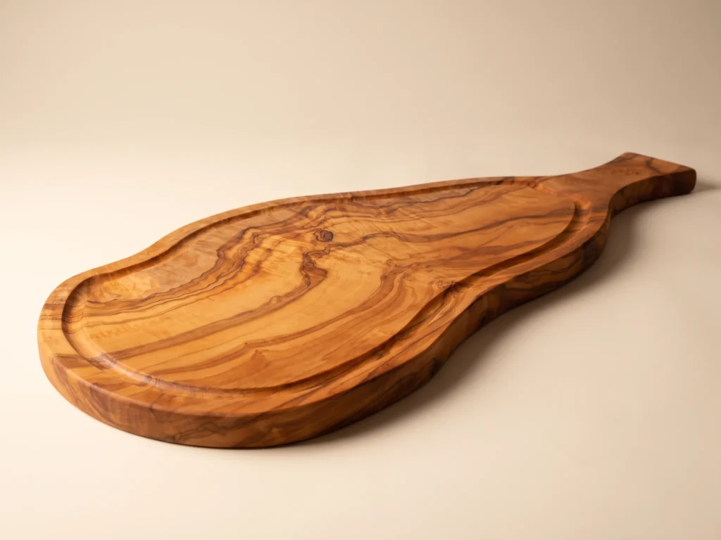 Natural shaped olive wood cutting board with juice groove and handle low three-quarter view
