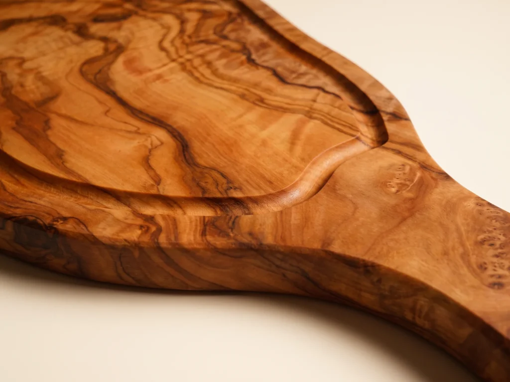 Natural shaped olive wood cutting board with juice groove and handle macro detail of groove and handle