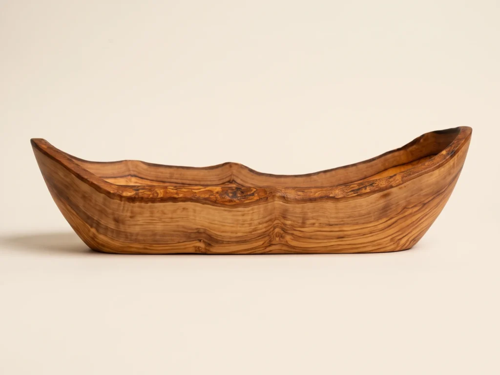 Side elevation view of rustic olive wood bread basket showing undulating silhouette and stable base