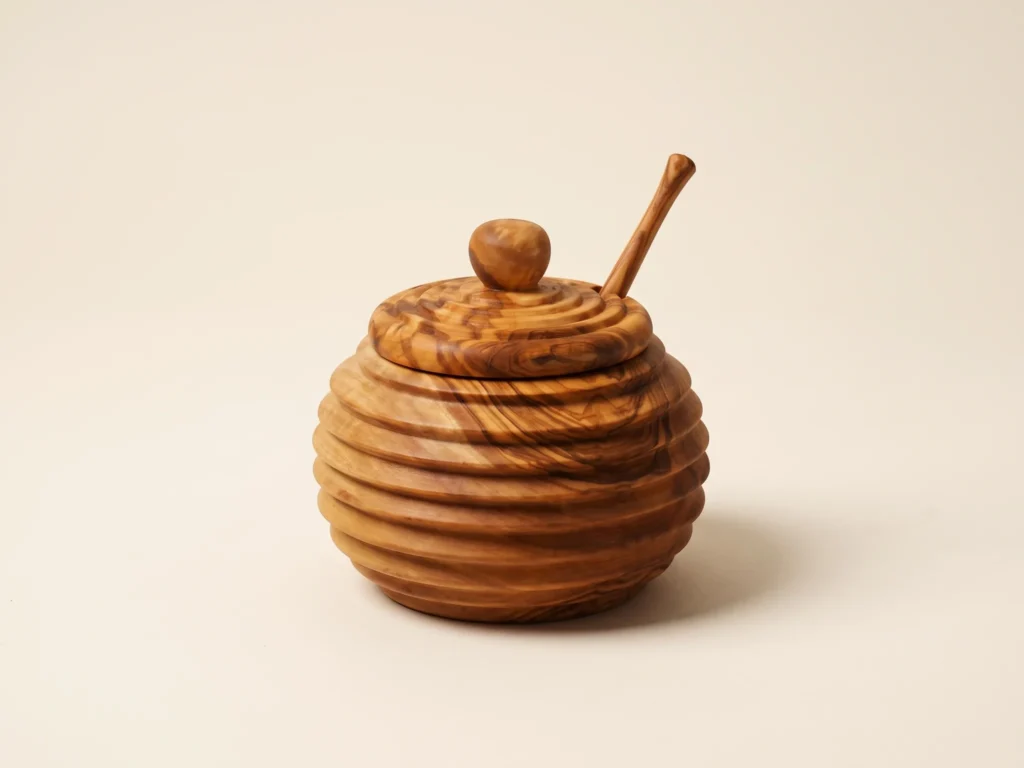 Three-quarter technical view of handcrafted olive wood honey jar with matching dipper