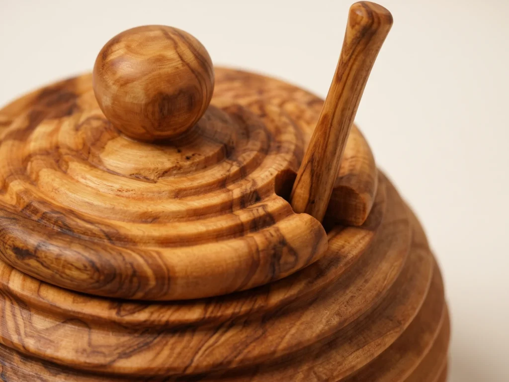 Macro detail view of olive wood honey jar concentric lid grooves, dipper notch, and grain ribbons