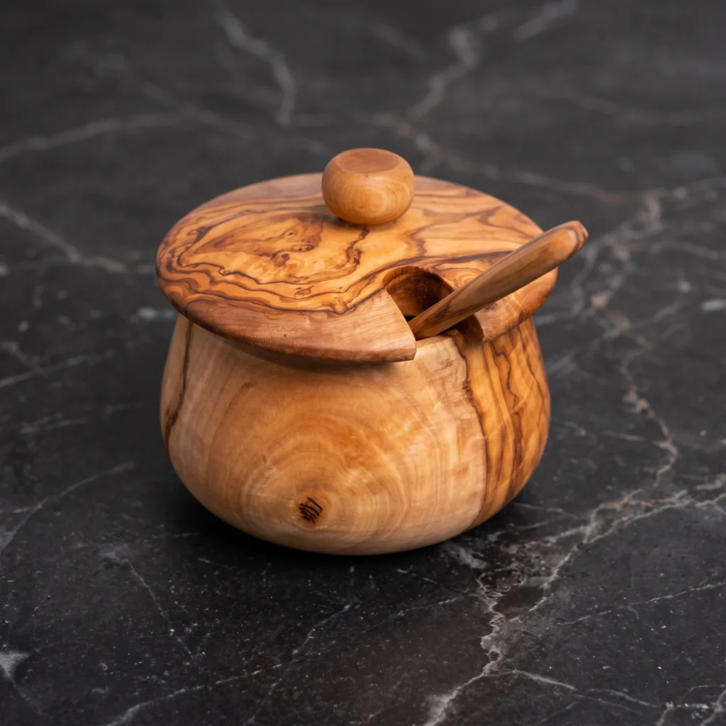 Handcrafted round olive wood sugar canister with domed lid and matching spoon on dark marble