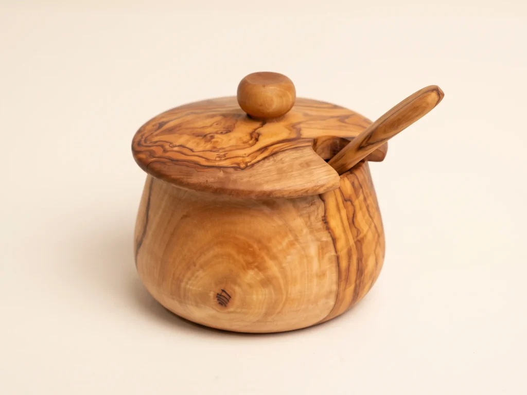 Olive wood sugar canister seen from a low three-quarter angle with its lid, knob and spoon