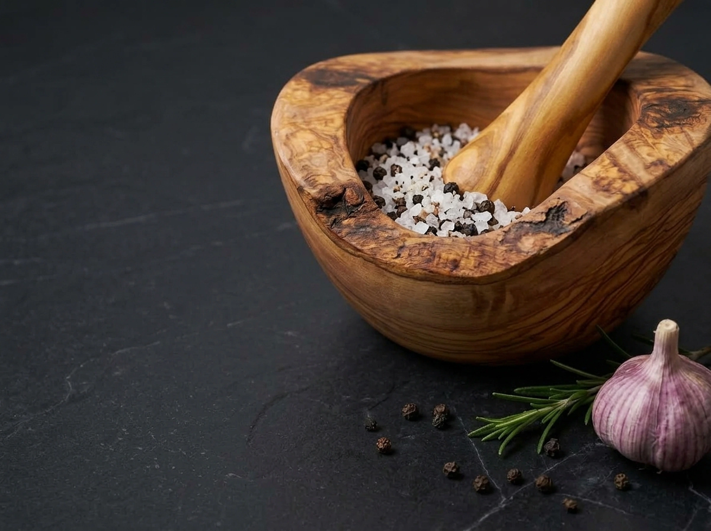 Handcrafted olive wood mortar with pestle and sea salt on dark slate